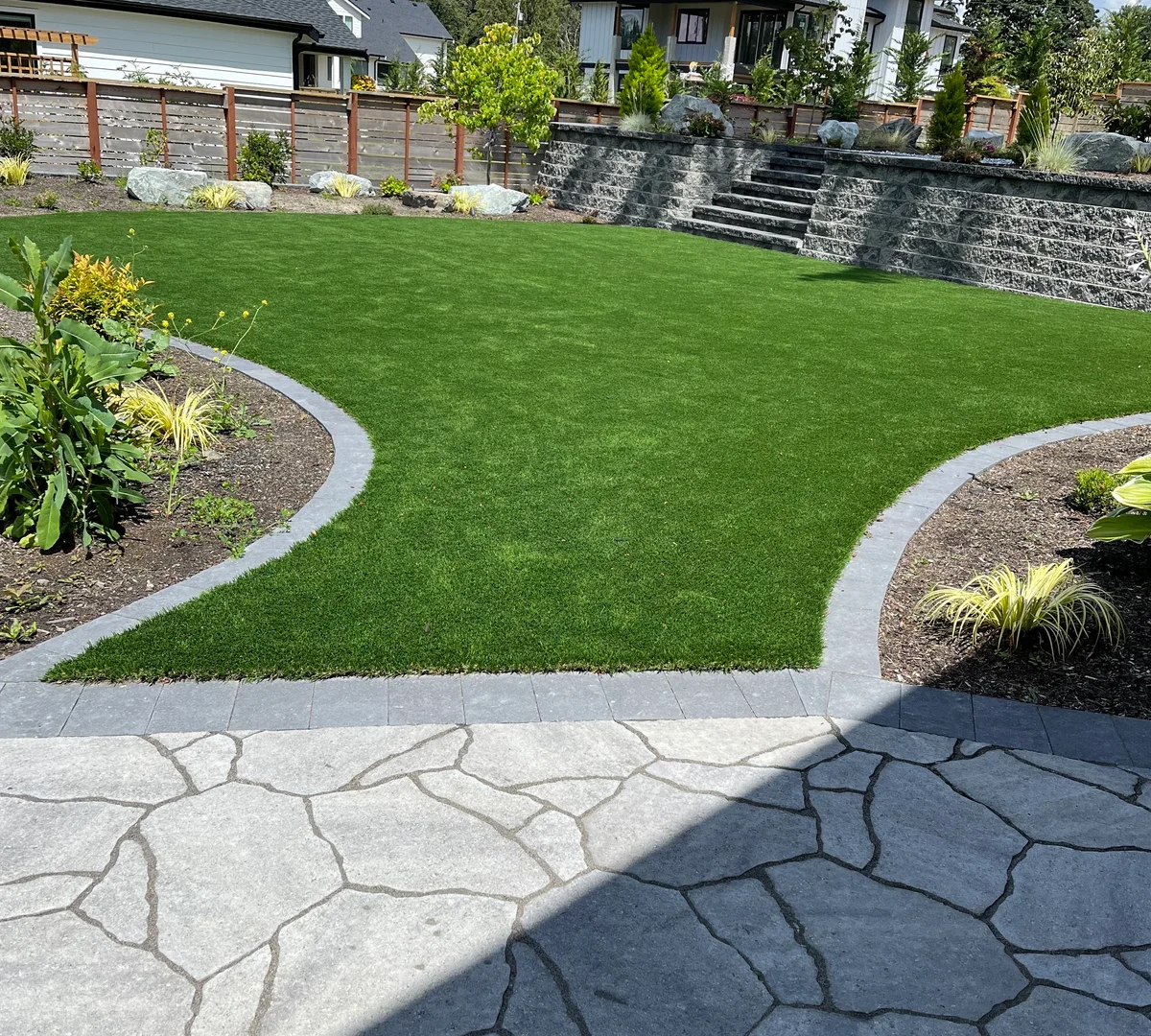 Finished backyard with flagstone patio, artificial turf, and stone retaining wall