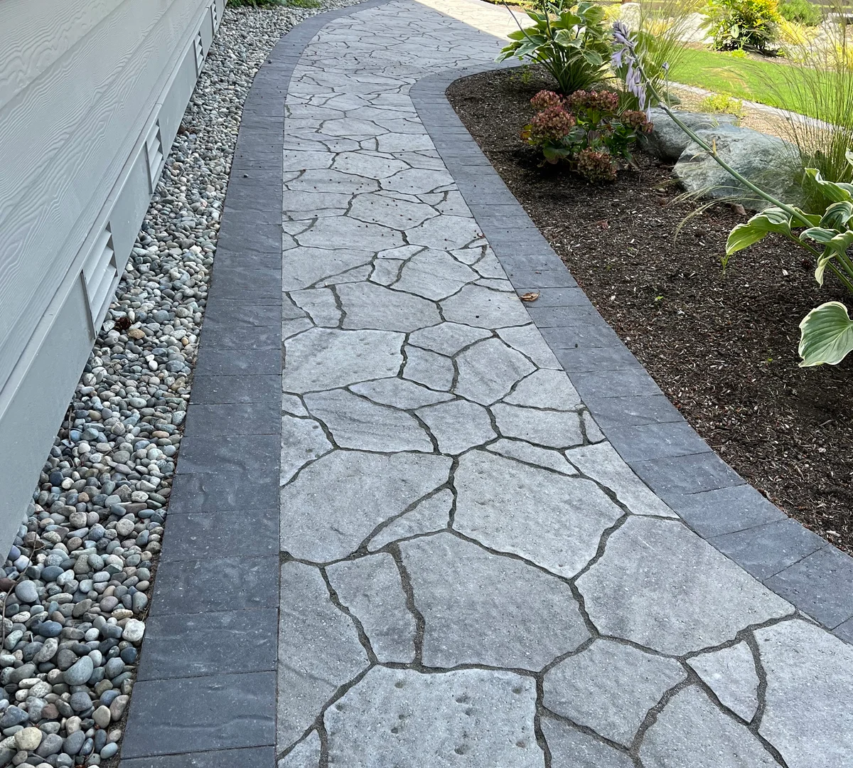 Curved flagstone walkway with dark border pavers and river rock edging